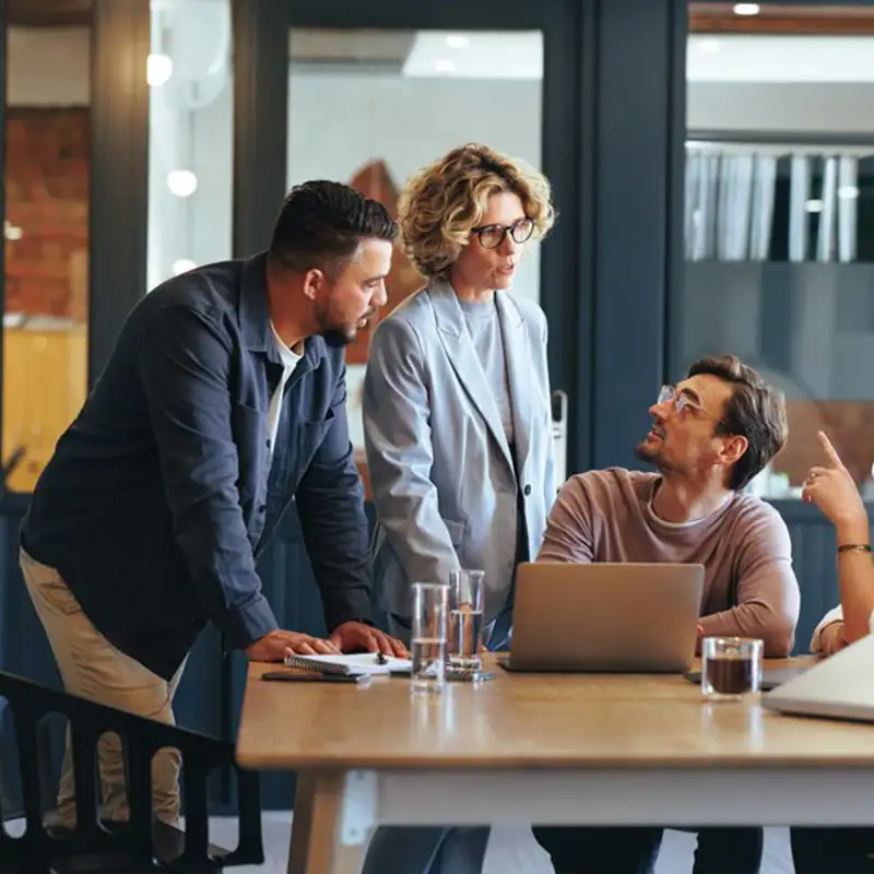 A group of coworkers talking at a desk in the office.