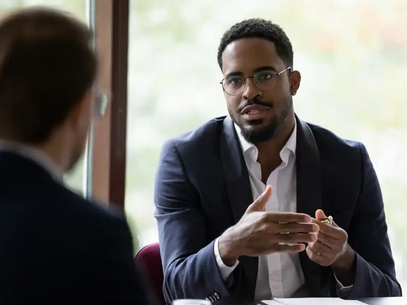 A man at a desk is giving an explanation to other person