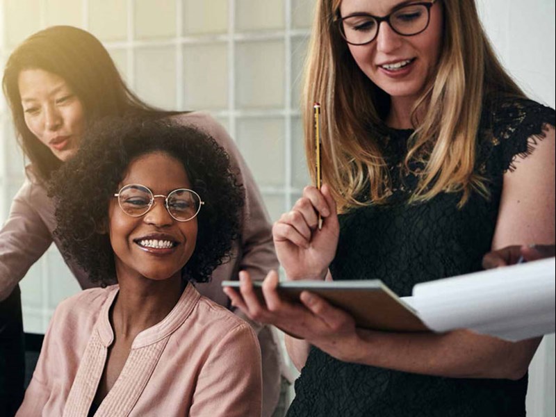 Group of female coworkers looking at paperwork laughing.