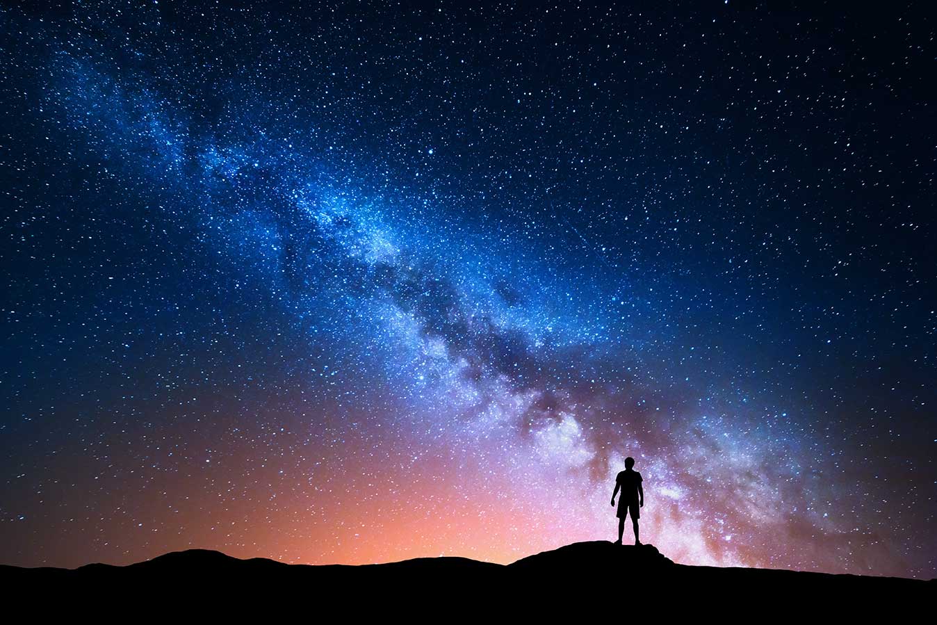Man standing on top of a mountain looking at the Milky Way at night.