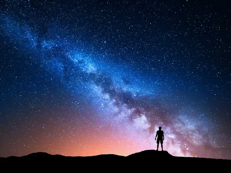 Man standing on top of a mountain looking at the Milky Way at night.